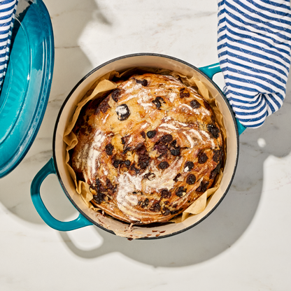 A baked Cherry Chocolate Sourdough Loaf in a heavy pot on a marbled surface.